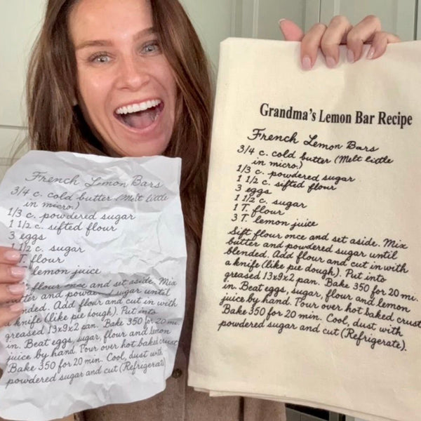 Woman holding a handwritten recipe and a natural tea towel with the cleaned up recipe image printed on it. The Printed Gift