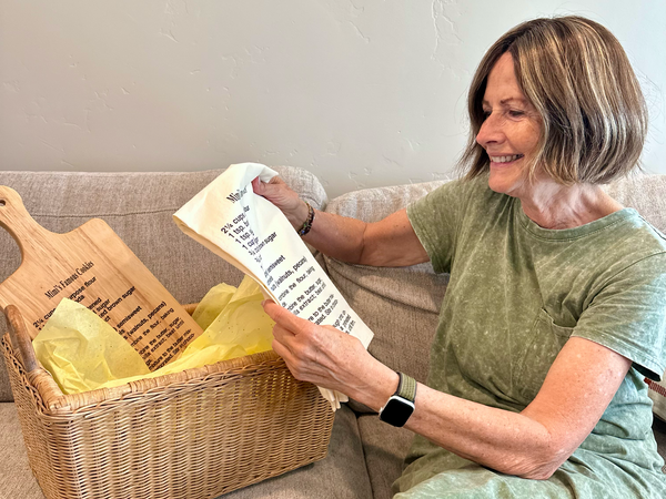 Women holding a custom handwritten recipe tea towel next to a basket with a family recipe cutting board